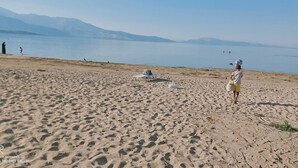 A sandy beach with footprints, a white chair, and a person carrying a child. - Hannapart Otel (Egirdir)