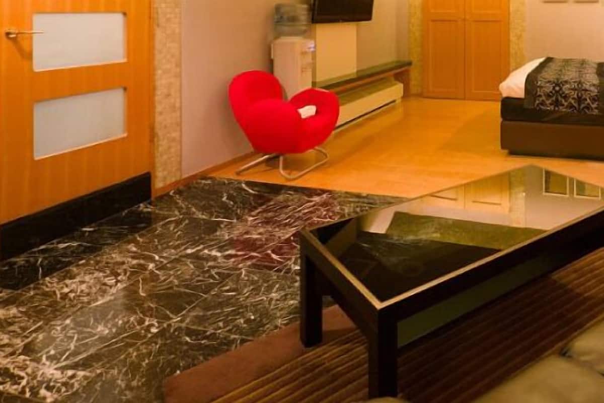 Une chambre d’hôtel avec un canapé, une table basse, un lit et un fauteuil rouge en forme de cœur.