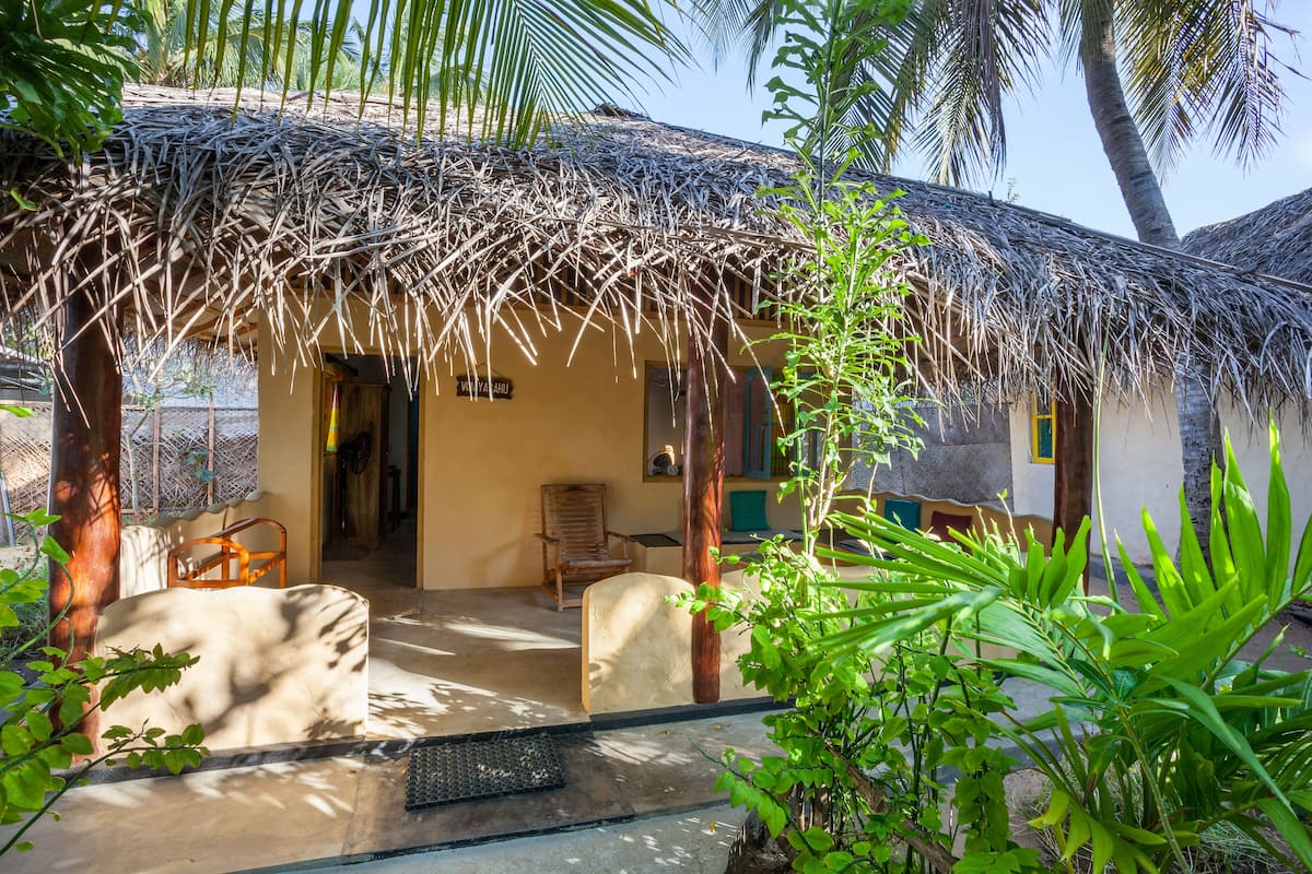 A thatched-roof structure with a concrete floor, a wooden chair, and a potted plant.