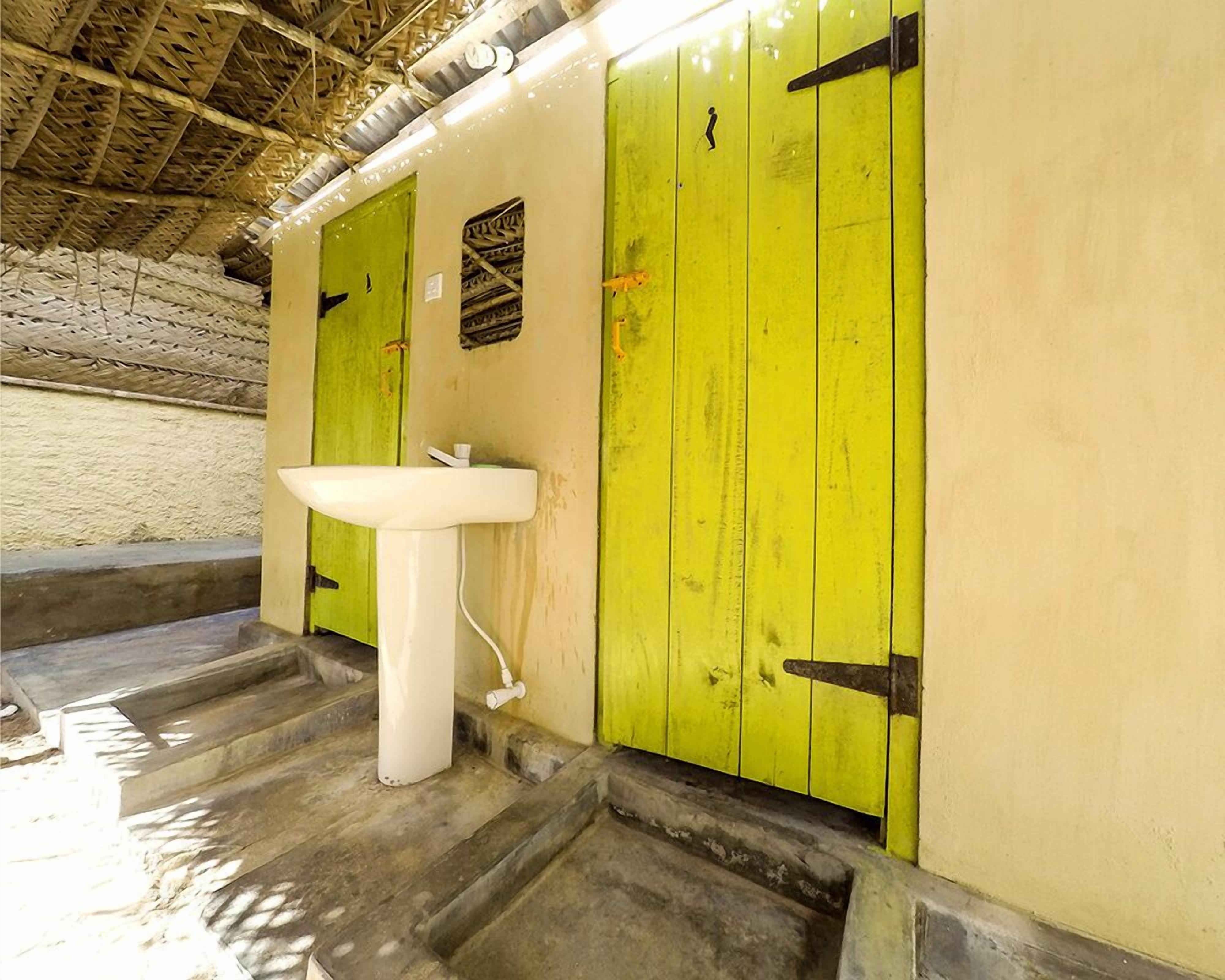 Un baño con lavamanos blanco, puertas verdes y techo de paja.