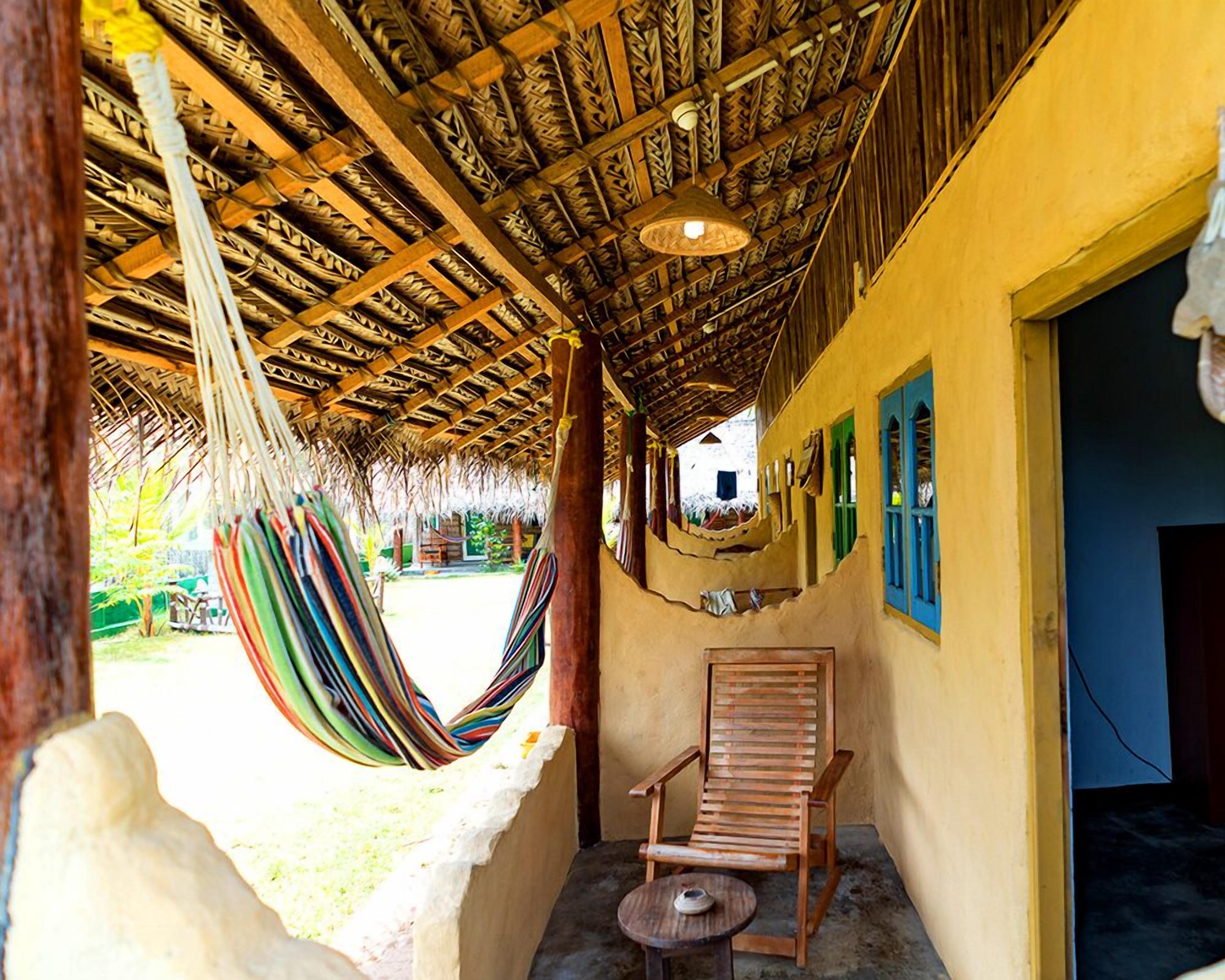 A room with a thatched roof, a hammock, a wooden chair, and a small table.