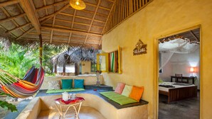 A room with a thatched roof, a hammock, a sofa with colorful cushions, a small table with a red napkin, and a bed with a wooden headboard. - De Silva Windresort Kalpitiya (Kalpitiya)