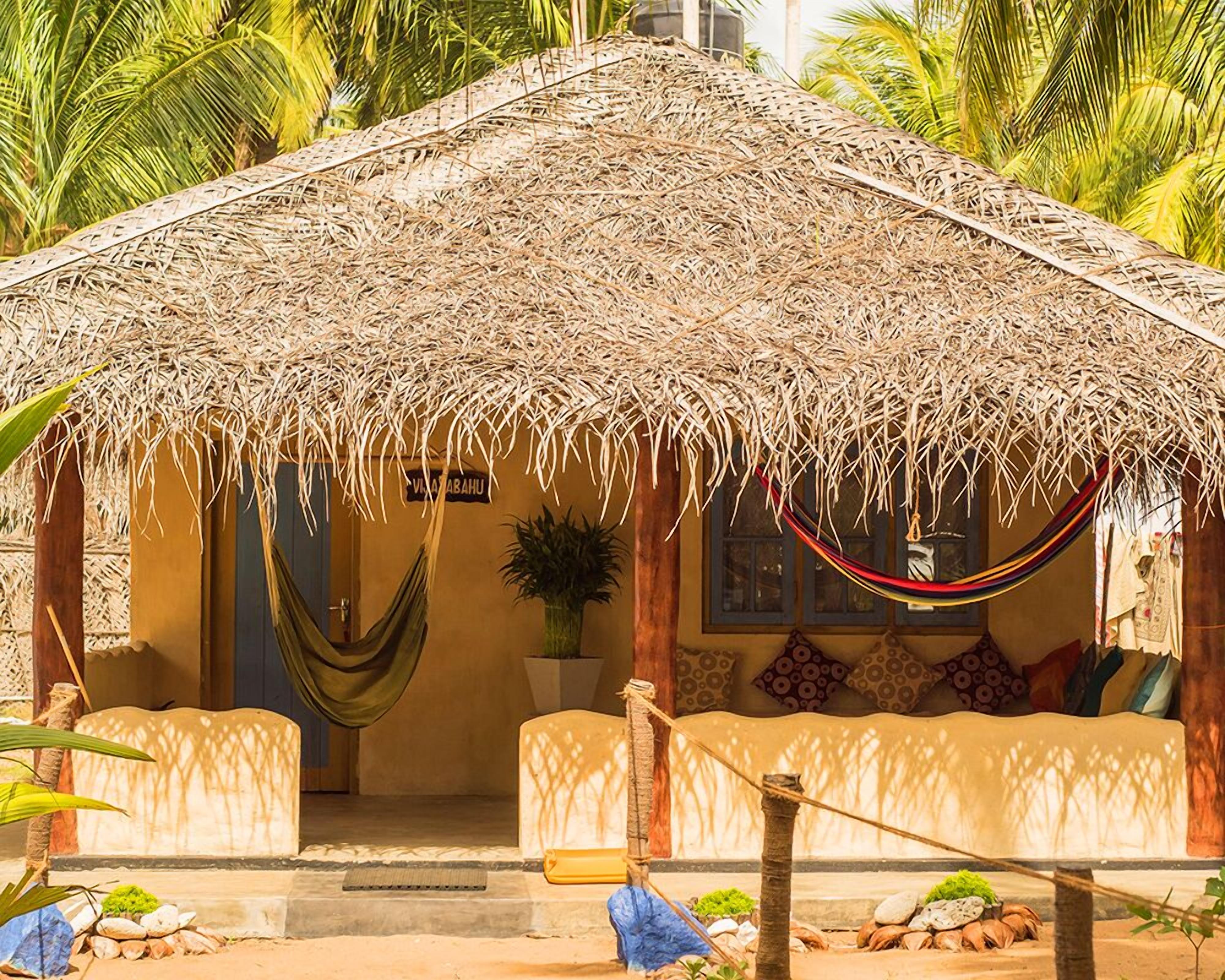 Uma cabana com telhado de palha, com uma rede, um sofá e uma placa que diz 'VILLA ABAHU'.