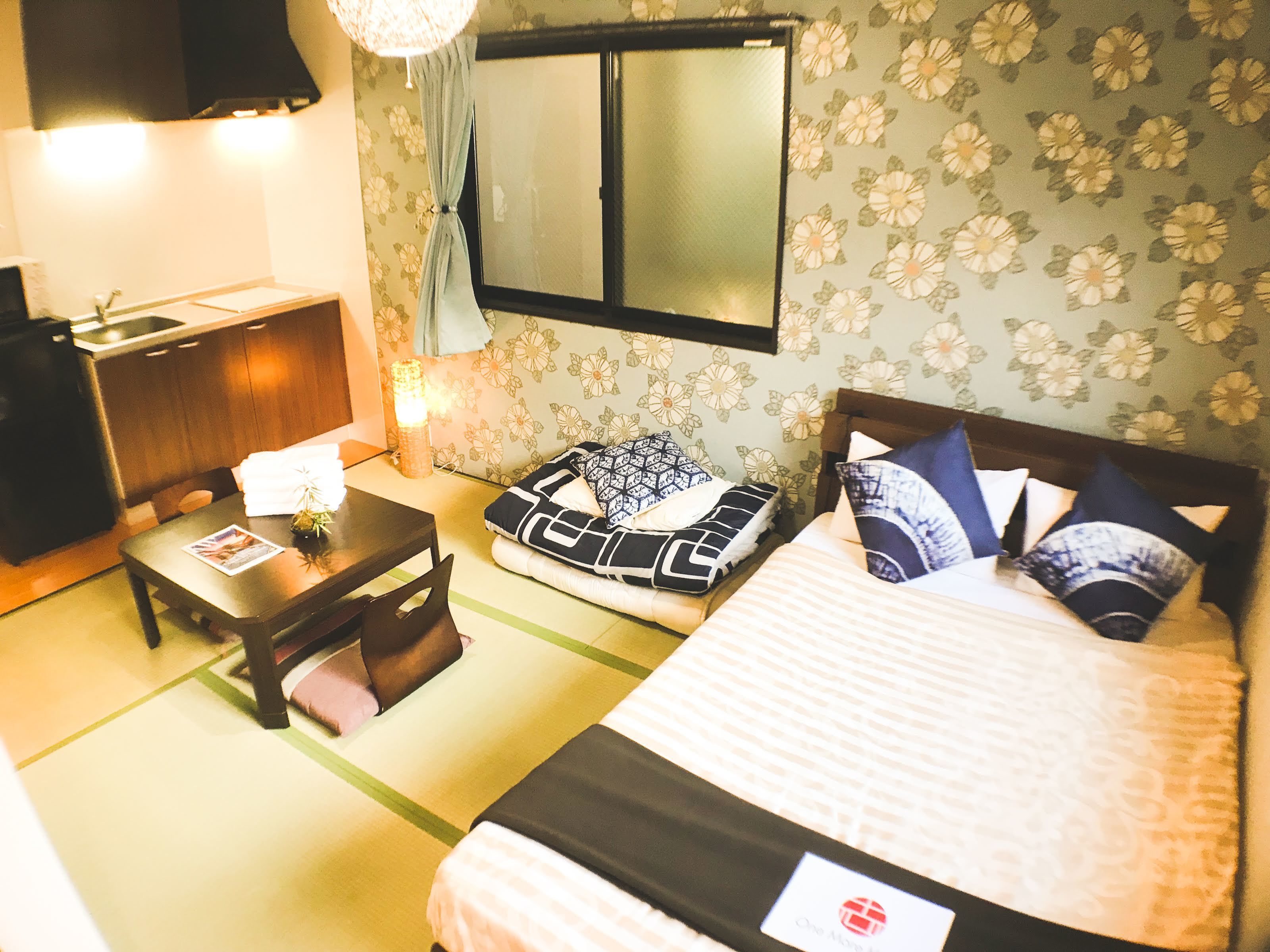 A hotel room with a bed, a desk, a chair, a small table, and a window with curtains.