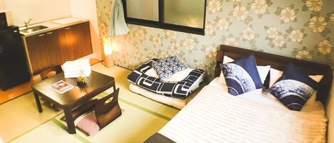 A hotel room with a bed, a desk, a chair, a small table, and a window with curtains.