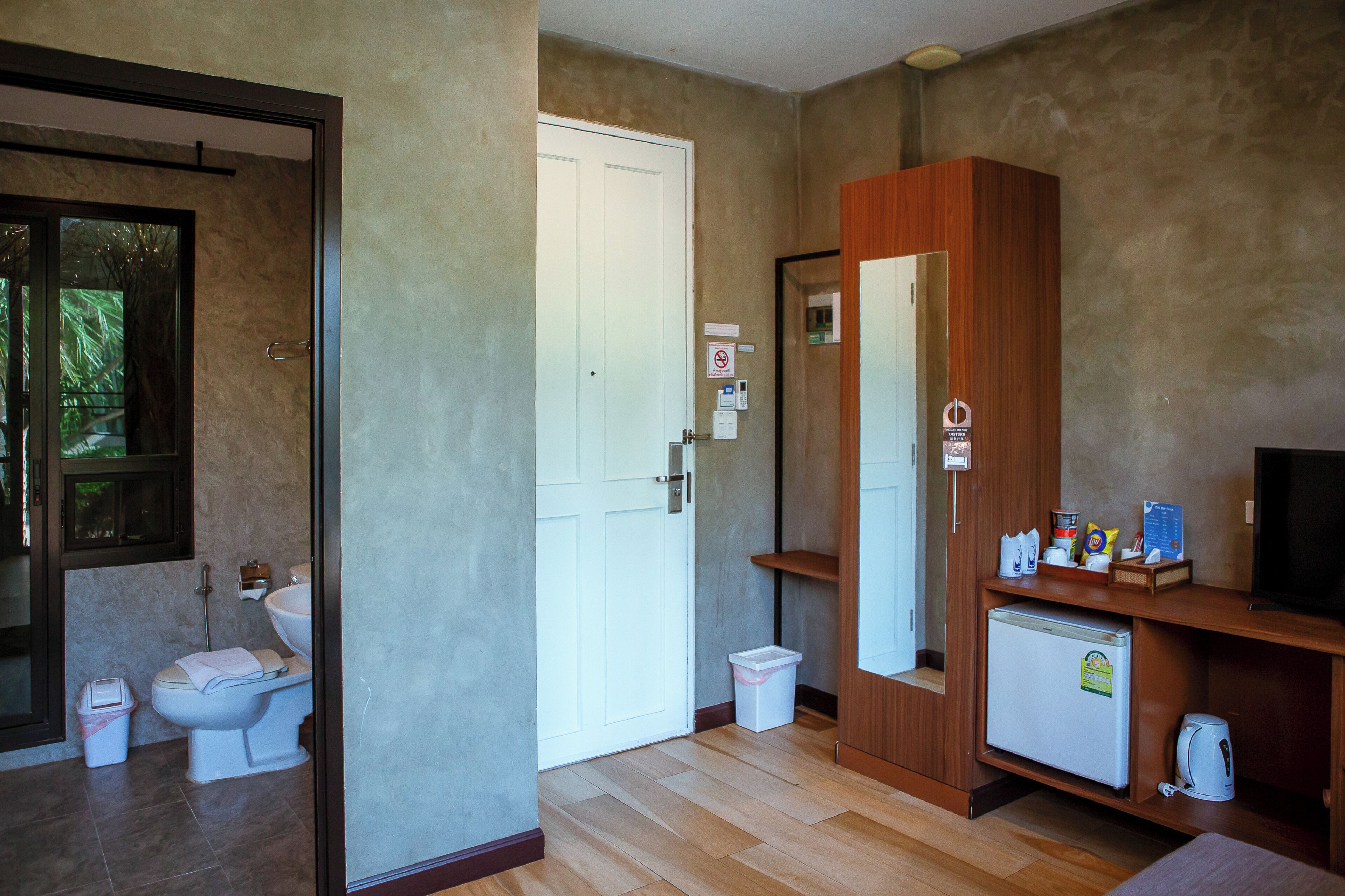 A bathroom with a toilet, sink, and shower. There is a wooden cabinet with a mirror and a small refrigerator.