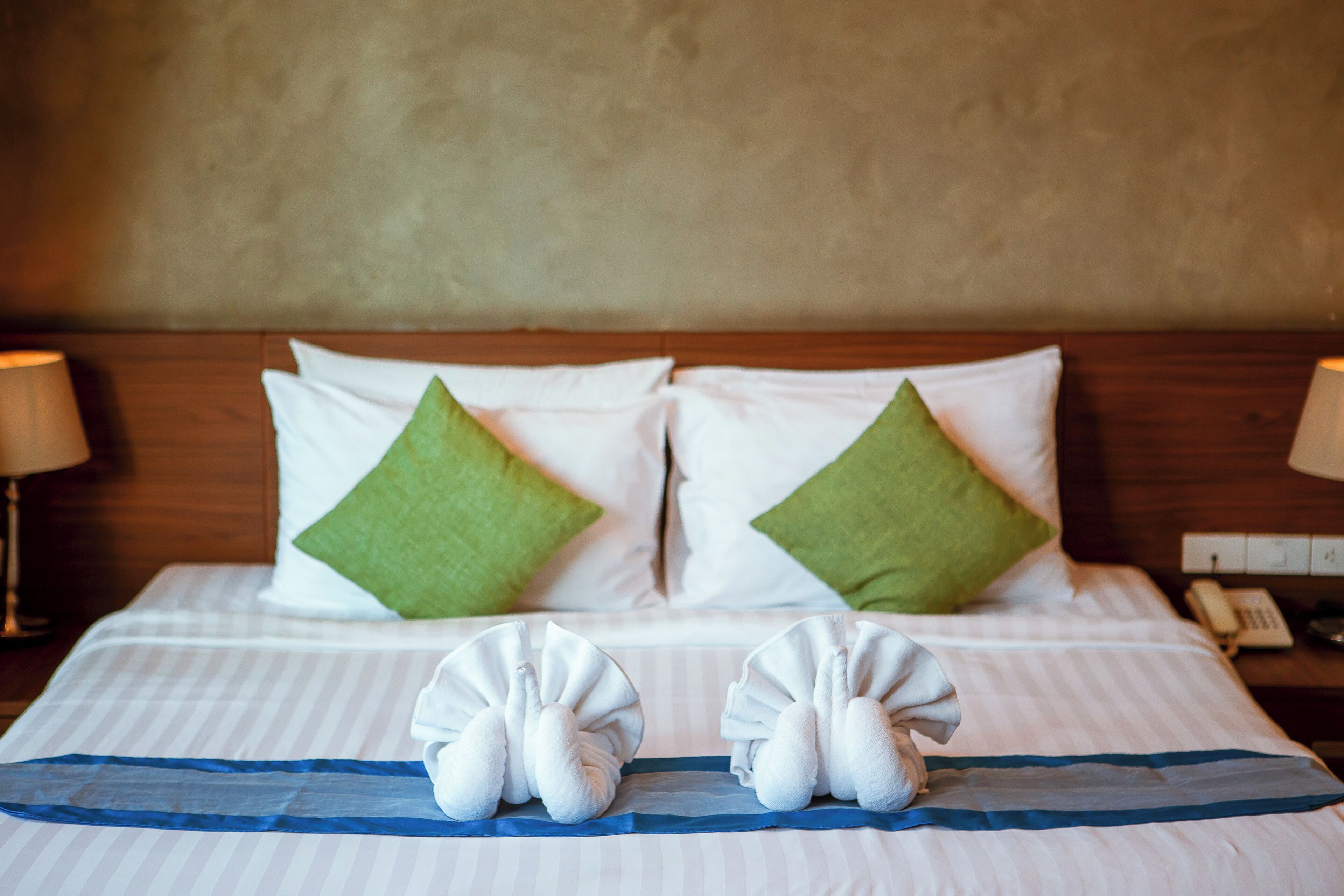 A neatly made bed with white and green pillows, a blue-striped bedspread, and two towels arranged on the bed.