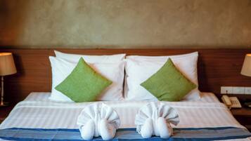 A neatly made bed with white and green pillows, a blue-striped bedspread, and two towels arranged on the bed.