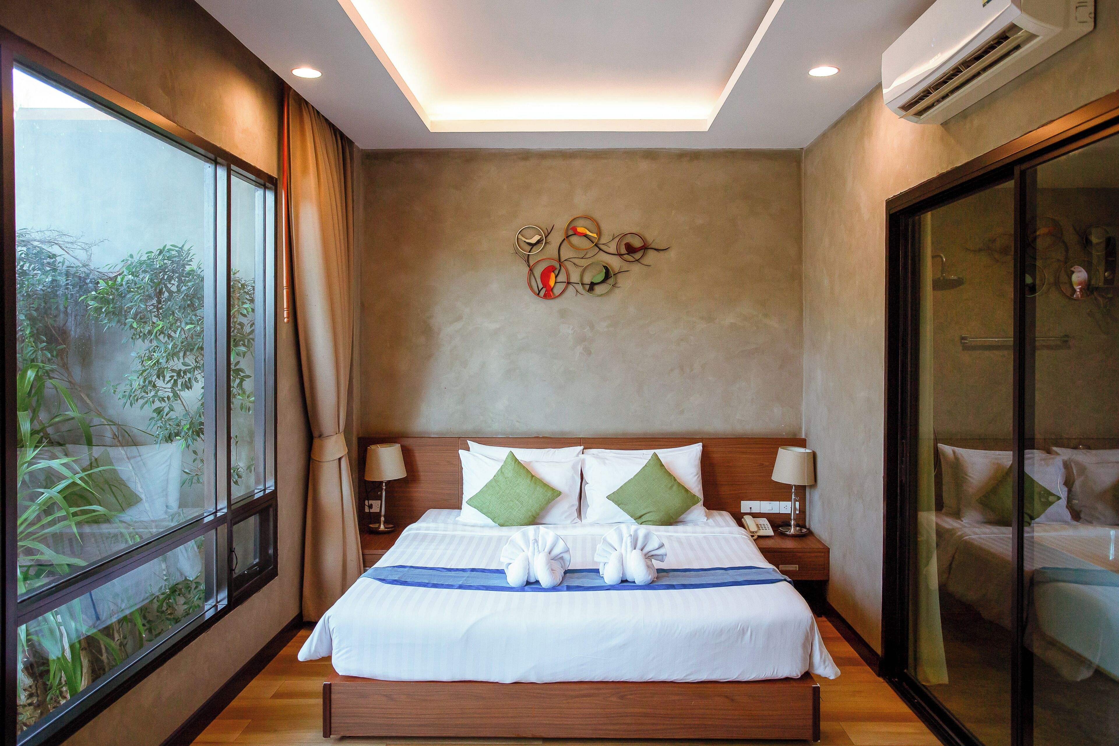 A hotel room with a large bed, two bedside tables with lamps, a wall-mounted artwork, and a sliding glass door to the right.