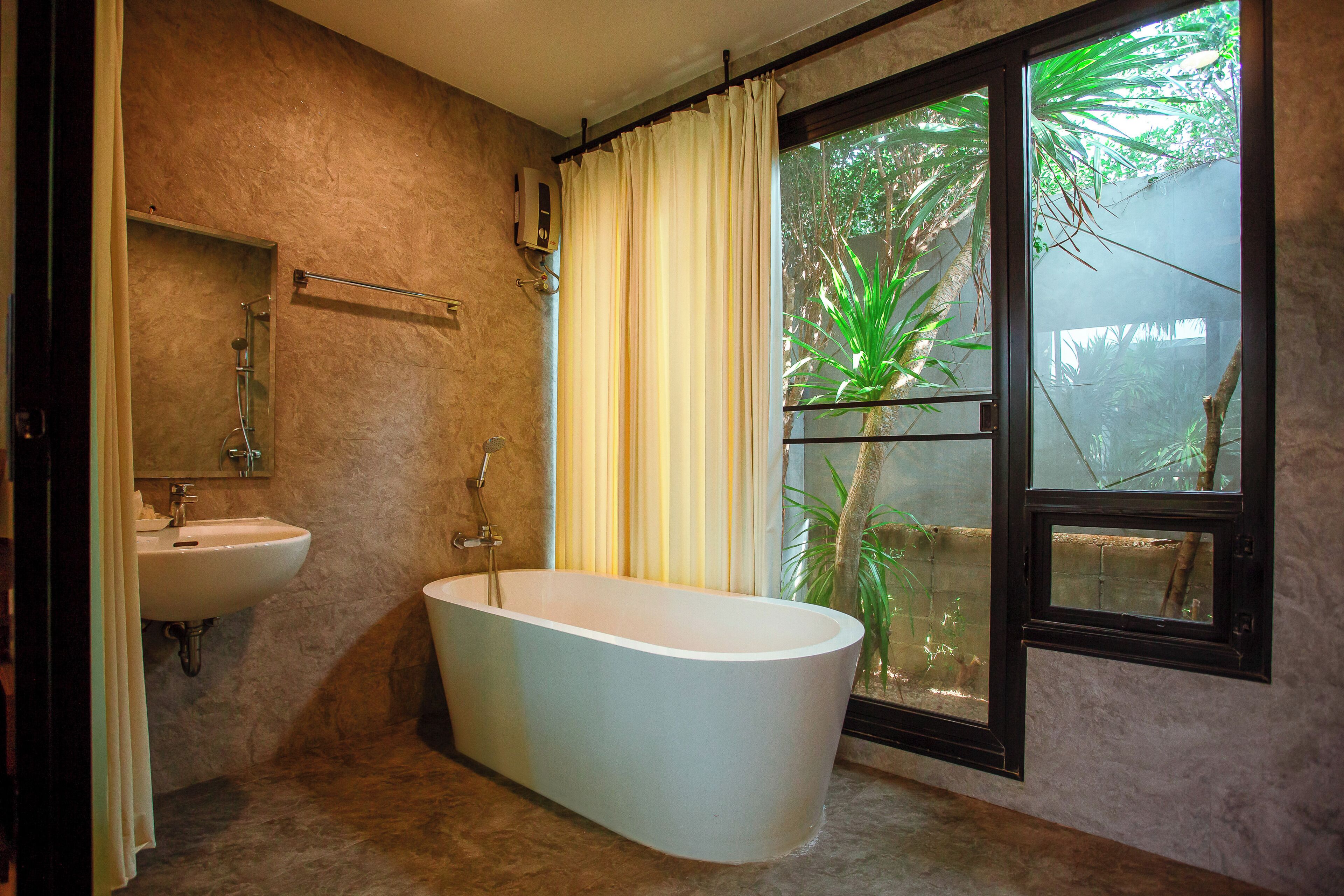 A bathroom with a freestanding bathtub, a sink, and a window with a view of greenery.