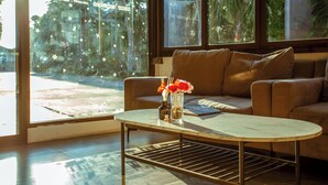 Quarto com sofá, mesa de centro e janela com vista para palmeiras e um prédio com relógio.