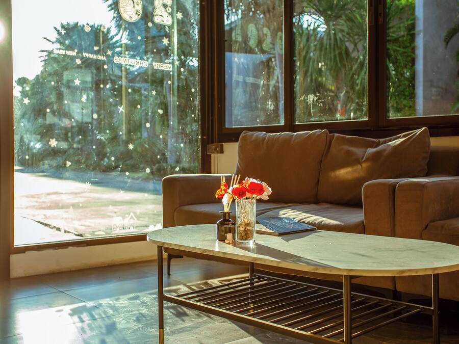 A room with a sofa, a coffee table, and a window with a view of palm trees and a building with a clock.