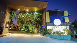 Entrada do Blue River Resort, com uma grande placa iluminada, uma galeria coberta e vegetação exuberante.