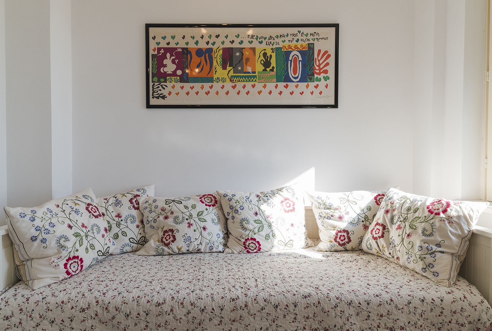 A room with a sofa bed, floral-patterned cushions, and a framed abstract artwork on the wall.