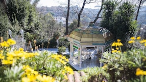 A gazebo with a tiled roof and white columns, surrounded by greenery and yellow flowers. - Casale dell'Insugherata B&B Roma (Rome)