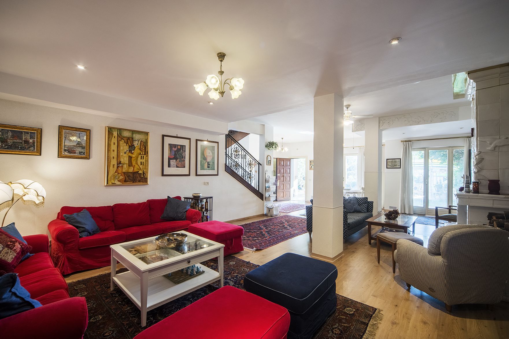 A spacious living room with a red sofa, a glass coffee table, and a staircase leading to another level.