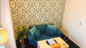 Una habitación pequeña con un sofá azul, una mesa de madera con un ratón de computadora, una lámpara y un papel tapiz estampado.