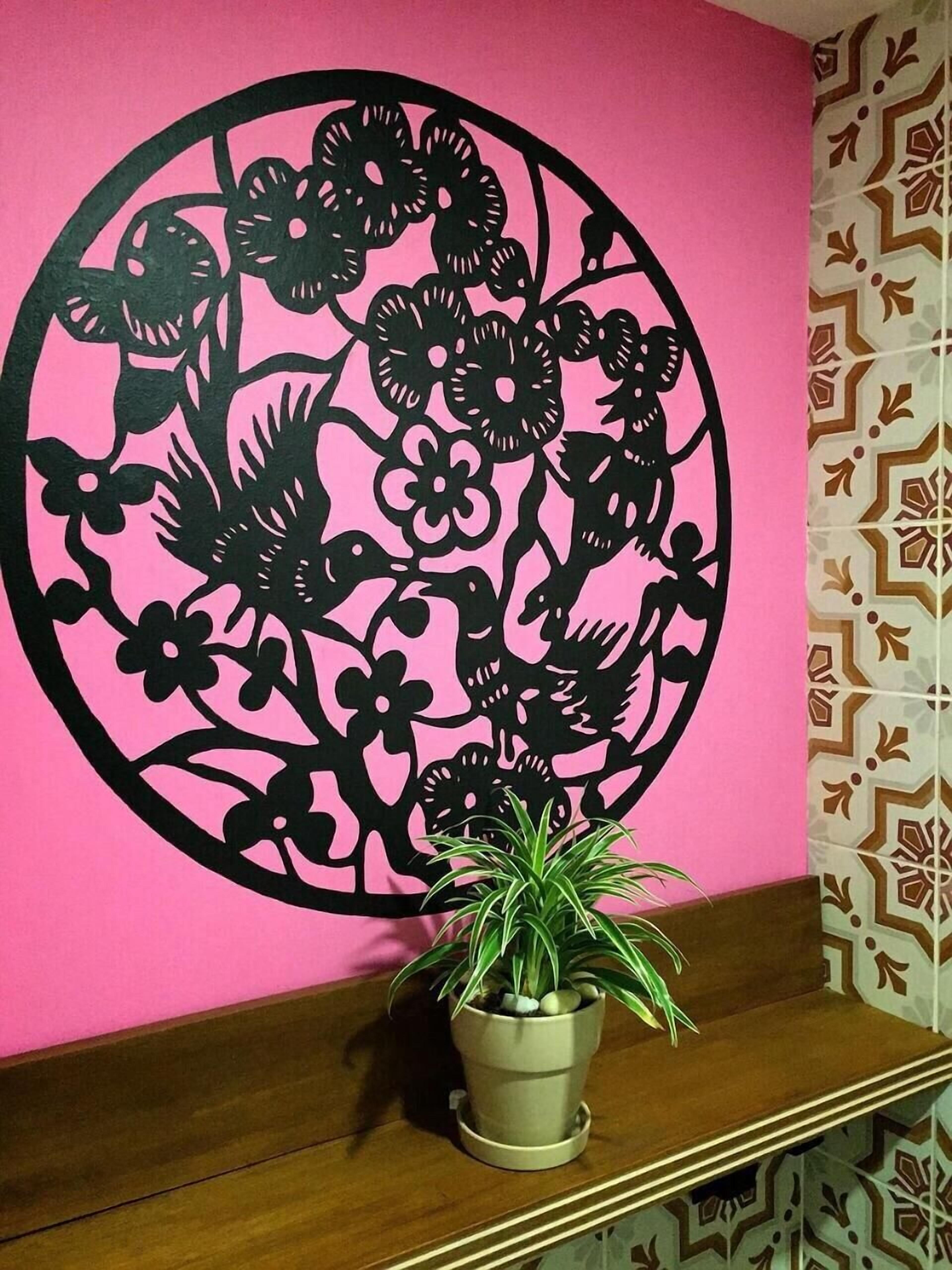 A wall with a large black floral cut-out design on a pink background.