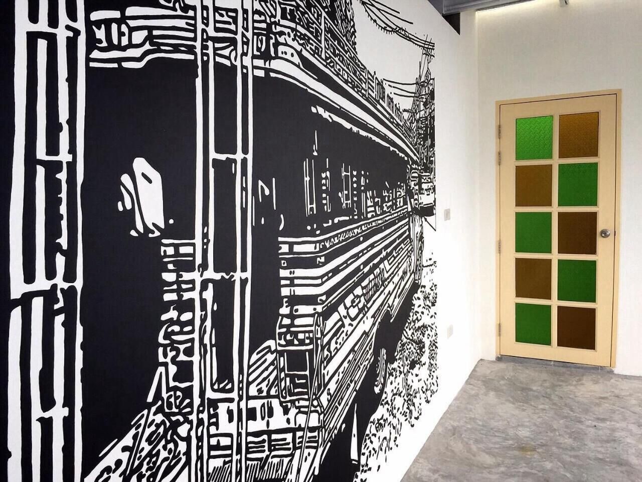 Un couloir orné d’une grande fresque murale en noir et blanc représentant un train, et une porte à panneaux verts.
