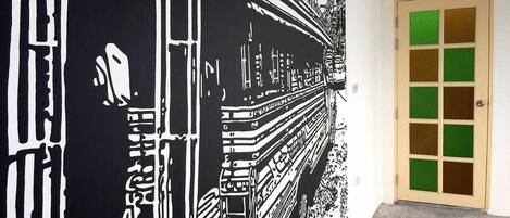 Un couloir orné d’une grande fresque murale en noir et blanc représentant un train, et une porte à panneaux verts.