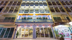 A hotel with multiple balconies, a central entrance with a sign, and a well-lit facade. - The Pho Thong Phuket (Phuket)
