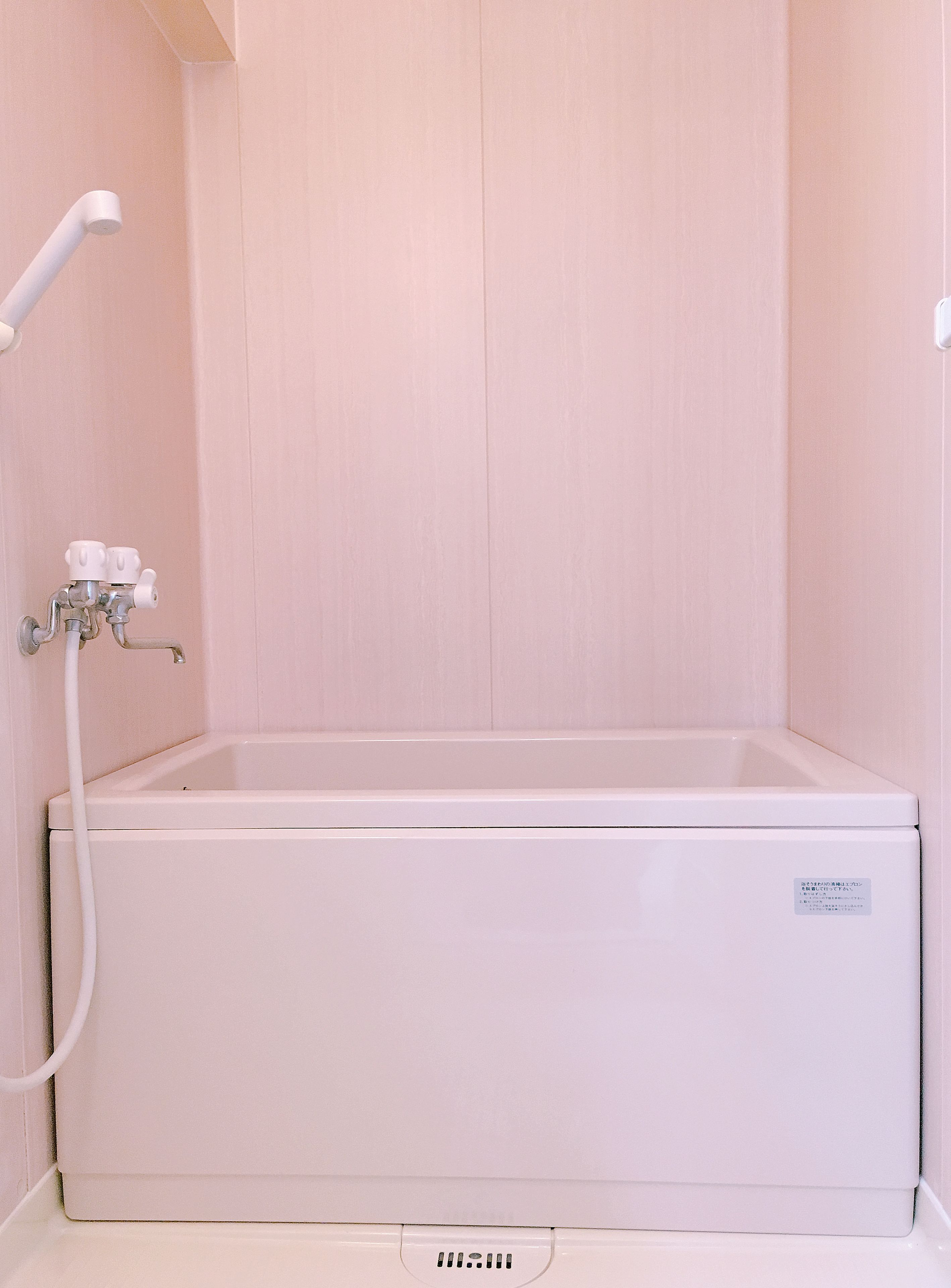 A white bathtub with a showerhead and control knobs, set against a plain wall.