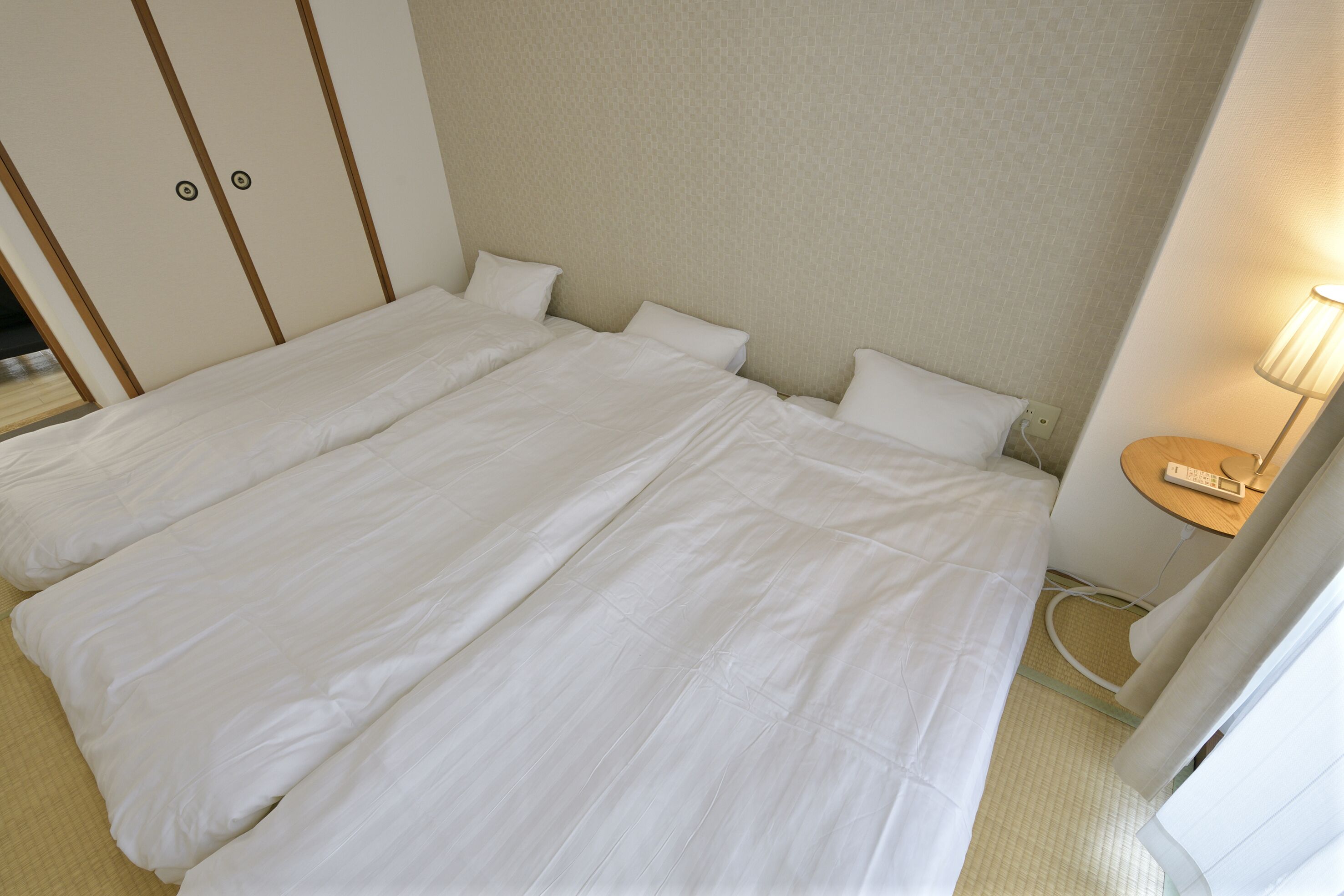 A hotel room with two beds, a bedside table with a lamp, and a wardrobe with a mirror.