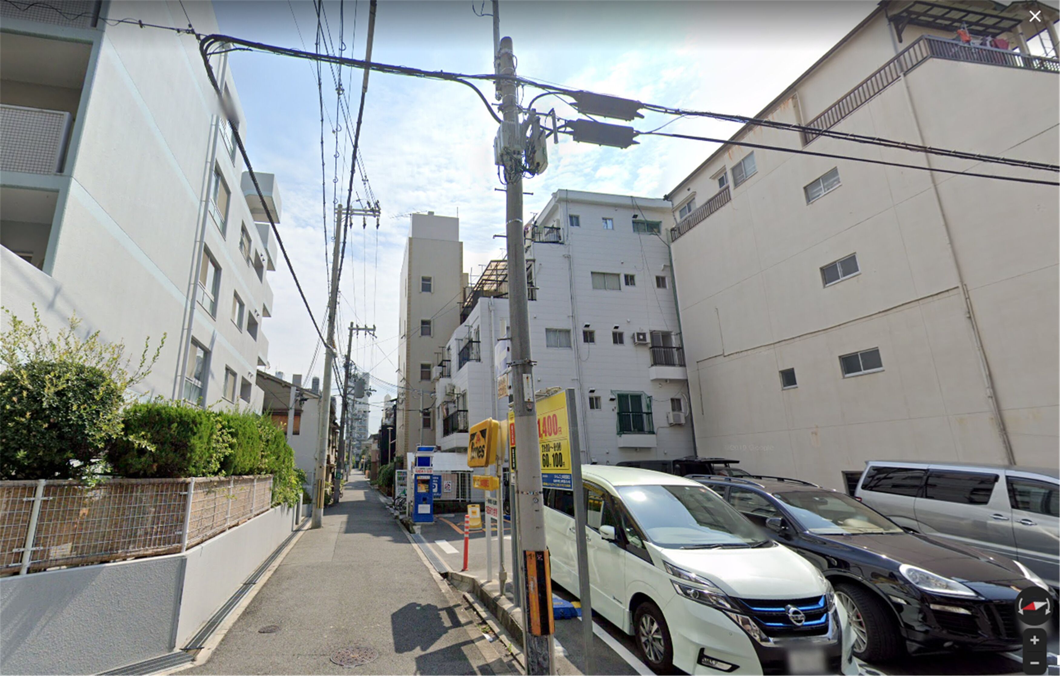 A narrow urban street lined with multi-story residential buildings, parked cars, and utility poles.