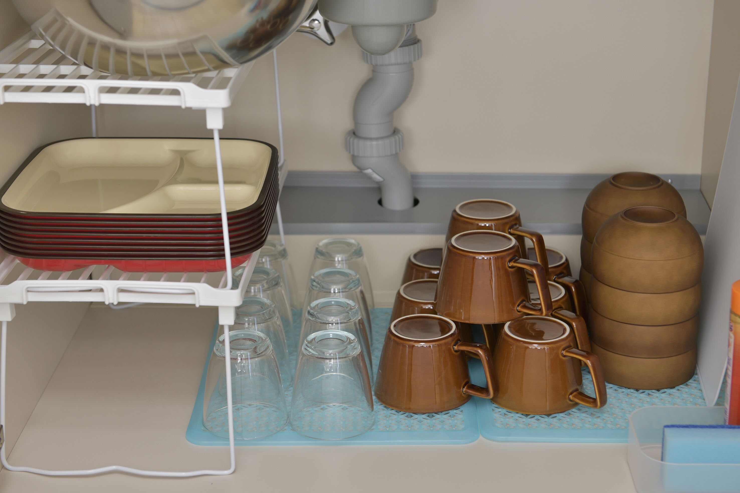 A kitchen with a dish rack, glassware, and brown mugs.