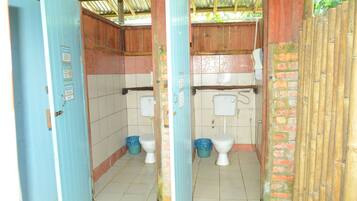 A small, enclosed bathroom with two toilets, a shower, and a tiled floor.