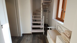 A spacious room with a wooden staircase, a built-in wardrobe, and a window with a view. - Agriturismo Podere Nigriano (Salò)