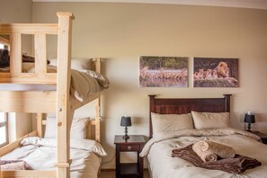 A hotel room with a bunk bed, a single bed, two nightstands with lamps, and two framed pictures on the wall.