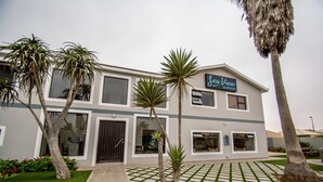 A modern building with a sign reading "Sea View Backpackers." It features a paved courtyard with palm trees and a well-maintained lawn. - Sea View Backpackers - Hostel (Swakopmund)