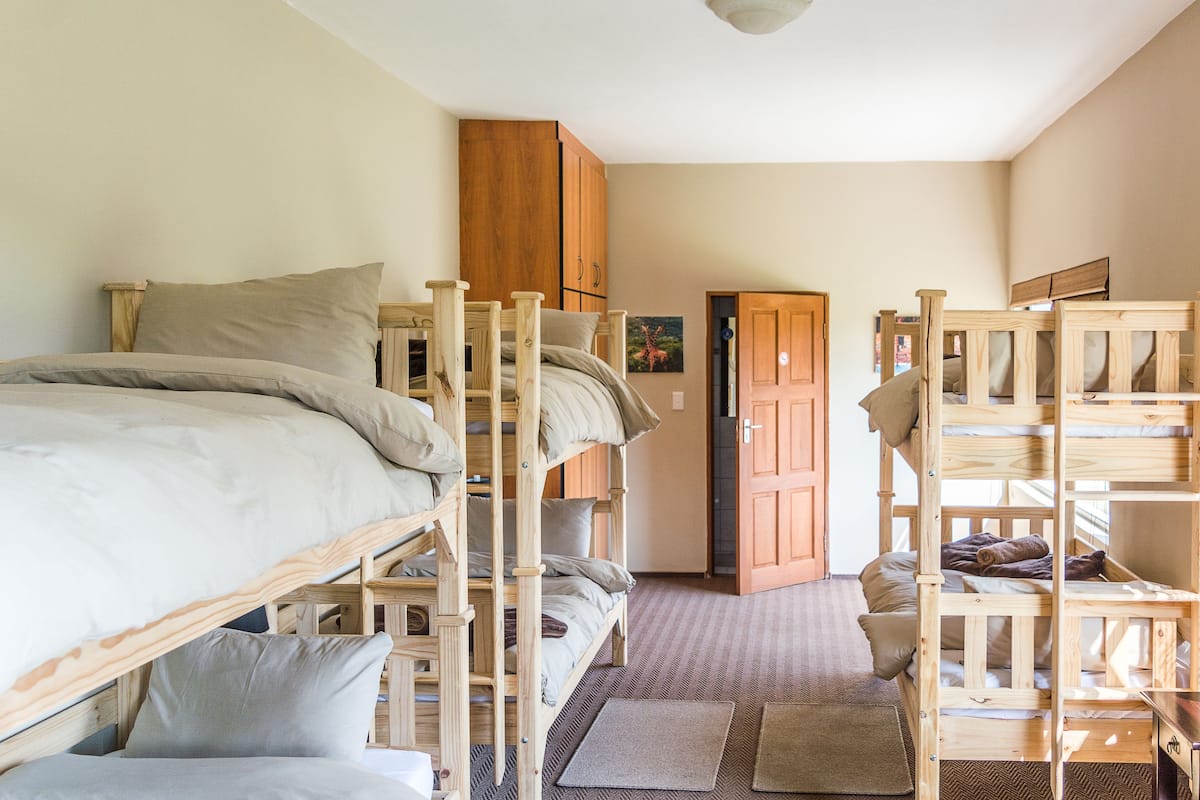 A dormitory-style room with bunk beds, a wooden wardrobe, and a door leading to another room.