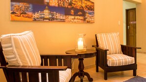 A room with two wooden chairs with striped cushions, a small table with a candle, and a painting of a building on the wall. - Sea View Backpackers - Hostel (Swakopmund)