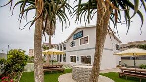 A courtyard with a stone fire pit, picnic tables, and umbrellas. - Sea View Backpackers - Hostel (Swakopmund)