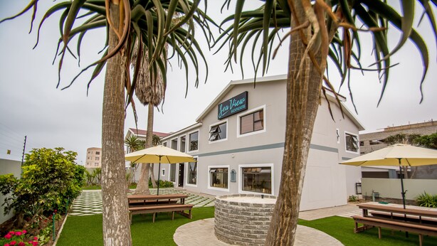 A courtyard with a stone fire pit, picnic tables, and umbrellas. - Sea View Backpackers - Hostel (Swakopmund)