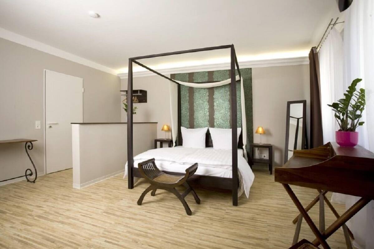 A bedroom with a four-poster bed, a wooden chair, a desk, and a potted plant.