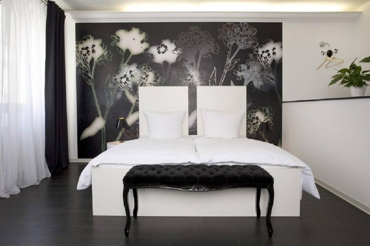 A modern bedroom with a large bed, white bedding, a black bench, and a floral wall mural.
