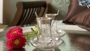A table with a clear glass pitcher and saucer, a red flower, and a patterned wall in the background. - Pension Mariposa (Weimar)