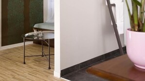 A room with a wooden floor, a glass table with a metal frame, a pink bowl on a wooden table, and a ladder leaning against the wall. - Pension Mariposa (Weimar)