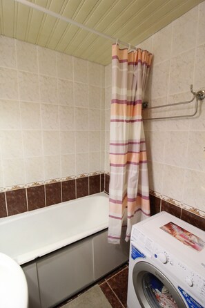 Bathroom features a bathtub, front-loading washing machine, and a striped shower curtain.