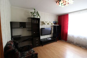 Relax in this inviting living room with a flat-screen TV, decorative shelf, and a potted plant.