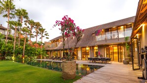 Un hotel moderno con piscina, mobiliario exterior y abundante vegetación.