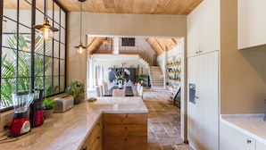 Una cocina amplia con encimera de mármol, armarios de madera y una isla central. Se ve una escalera que sube a un nivel superior, y la cocina está bien iluminada con lámparas colgantes.