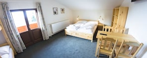 Un dormitorio con una cama de madera, un escritorio y una silla. Hay una ventana con cortinas, un radiador y una estantería con objetos.