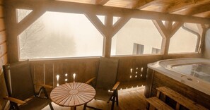 Una cabaña de madera con un jacuzzi, bancos de madera y una mesa con velas.