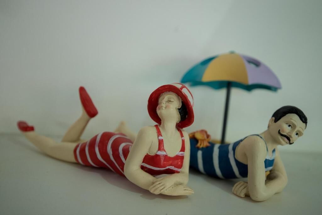 Two figurines lying on a flat surface with a colorful umbrella in the background.