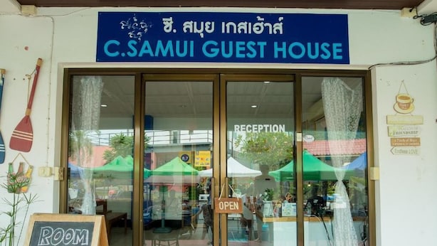 La entrada a C. Samui Guest House, con un área de recepción visible a través de las puertas de vidrio.