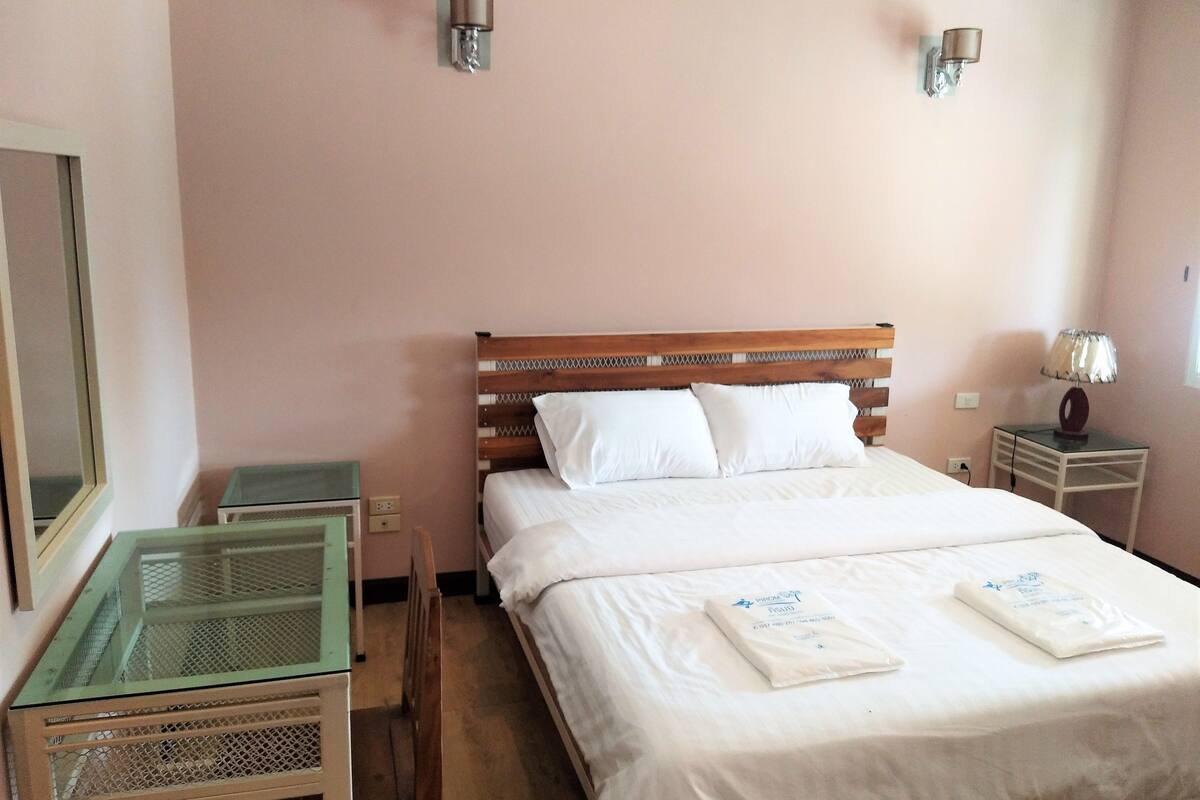 A neatly arranged hotel room with a wooden bed, white bedding, a glass table, and two wall-mounted lamps.